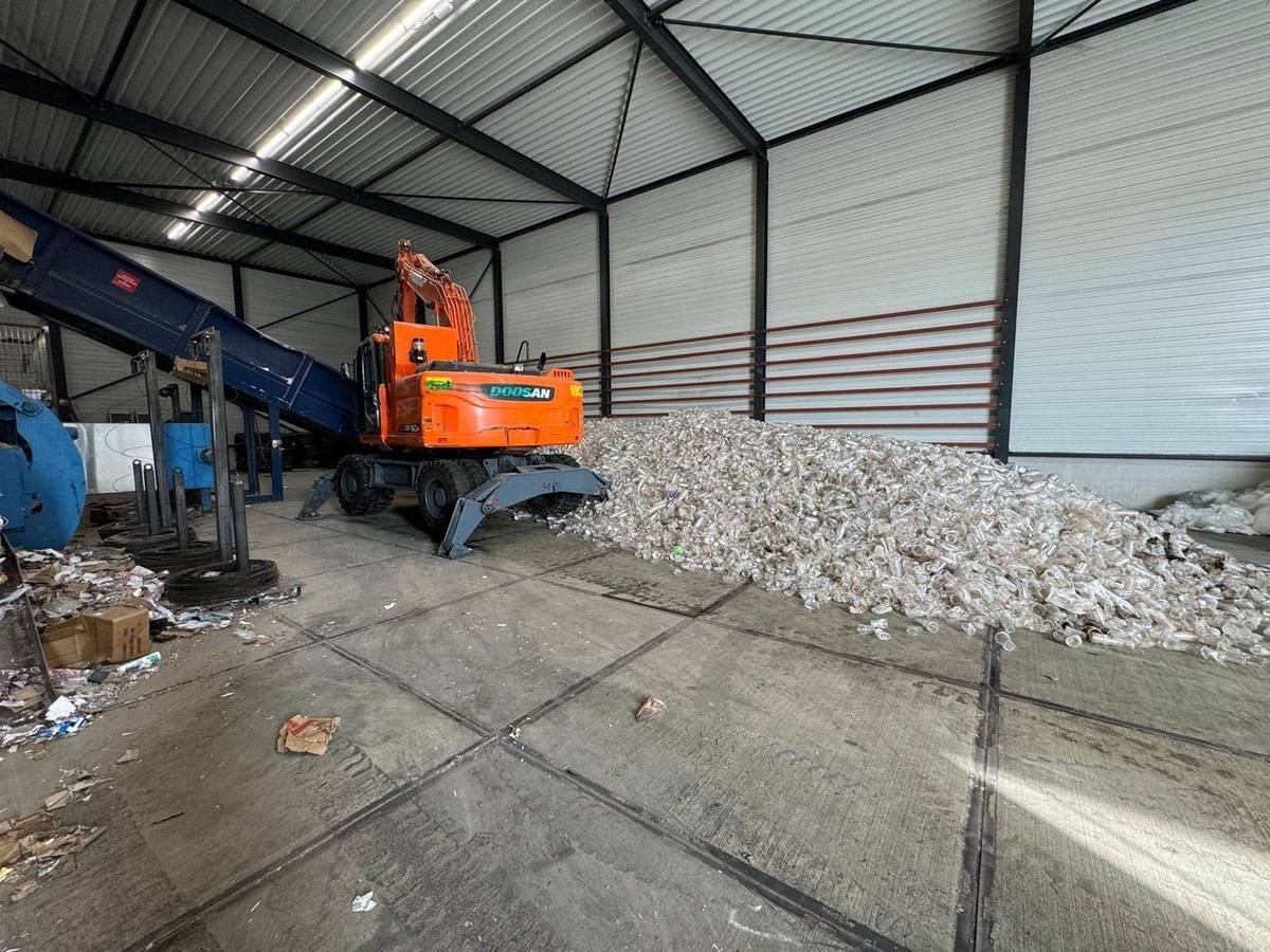 Ingezamelde bekers op de vloer van onze sorteerhal, met kraan en pers